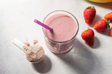 Strawberry and banana smoothie, protein drink in a glass, measuring scoop with whey protein powder,...