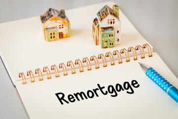 Remortgage - a word written in a notebook with a pen and a ceramic miniature of a house. Business...