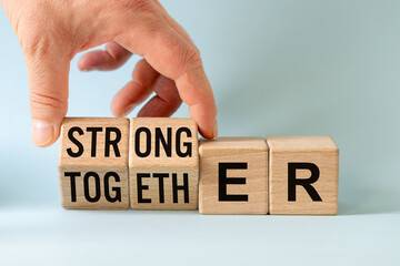 stronger together, businessman arranges the word stronger and together from wooden blocks, business...