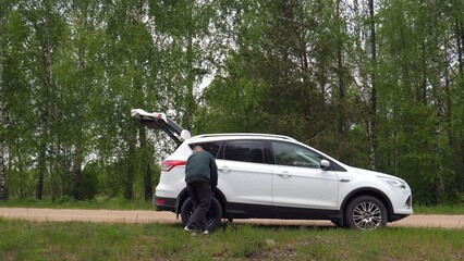 a man changes a broken tire on the side of a country road