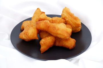 Patongko or Deep-fried dough sticks dish placed on white fabric. Patongko is a Thai dessert snack, for deep frying, breakfast, crispy texture, and Asia food concept. Food with white fabric background.