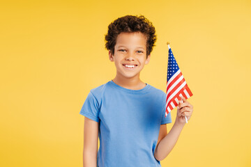Little, smiling African American boy, patriot holding American flag looking at camera