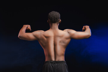 Back view of young pumped African American bodybuilder male athlete with bare torso