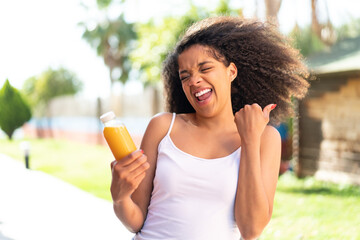 Young African American woman holding an orange juice at outdoors celebrating a victory
