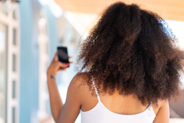 Young African American woman using mobile phone at outdoors in back position