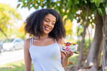 Young African American woman holding a bowl of fruit at outdoors with happy expression