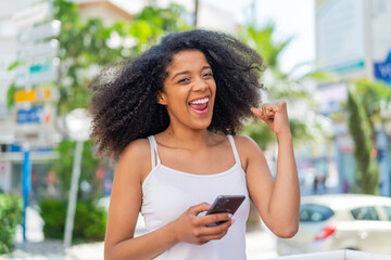 Young African American woman at outdoors with phone in victory position