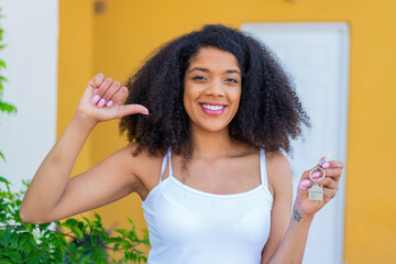Young African American woman holding home keys at outdoors proud and self-satisfied