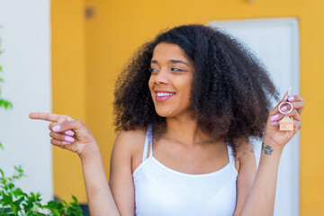 Young African American woman holding home keys at outdoors pointing to the side to present a product