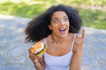 Young African American woman holding a burger at outdoors intending to realizes the solution while...