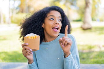 Young African American woman holding fried chips at outdoors intending to realizes the solution...
