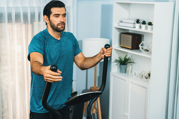 Athletic and sporty man running on elliptical running machine during home body workout exercise...