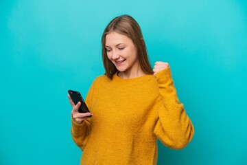 Young Russian woman isolated on blue background using mobile phone and doing victory gesture
