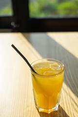 Closeup of fresh fruit juice in glass with straw and ice cubes on cafe table
