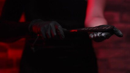 Close-up of female hands in black gloves holding a BDSM whip on a red background. Hits his hand with a whip. BDSM is an outfit for adult sex games. Sex shop Adult store
