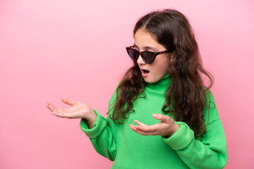 Little caucasian girl wearing sunglasses isolated on pink background with surprise facial expression