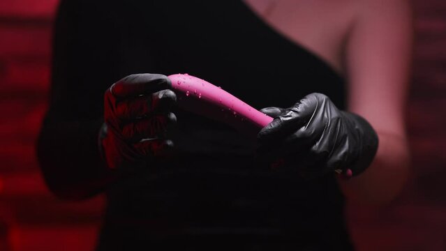 Burgundy stylish dildo for masturbation in the hand of a girl wearing black gloves on a red background. Nozzle for clitoral stimulation. Sex shop Adult store
