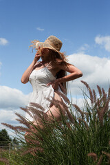 Young sexy beautiful woman in a straw hat stands in the garden against the background of the sky.