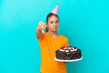 Little caucasian girl holding birthday cake isolated on blue background showing thumb down with...