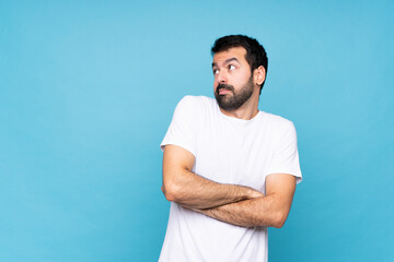 Young man with beard  over isolated blue background making doubts gesture while lifting the...