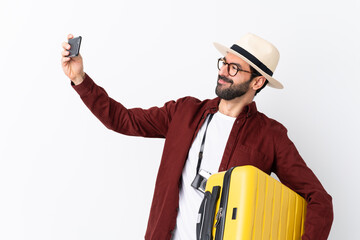 Traveler man man with beard holding a suitcase over isolated white background making a selfie