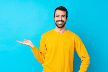 Young caucasian man over isolated blue background holding copyspace imaginary on the palm to insert an ad