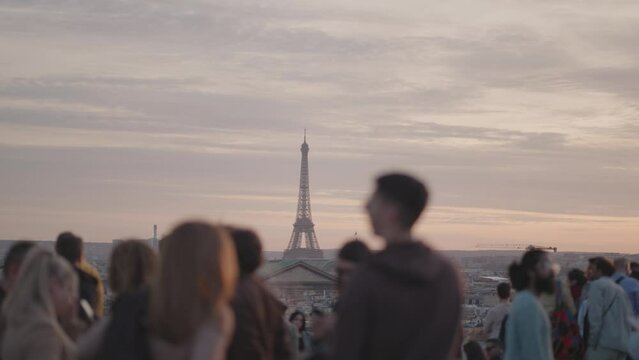 Unrecognizable Tourists on the rooftop of Galeries Lafayette Haussmann enjoying the sunset with the iconic Eiffel Tower and the city buildings of Paris in the background