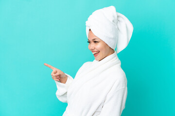 Teenager blonde girl in a bathrobe over isolated blue background pointing finger to the side and...