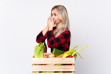 Farmer girl holding a basket full of fresh vegetables over isolated white background covering mouth...
