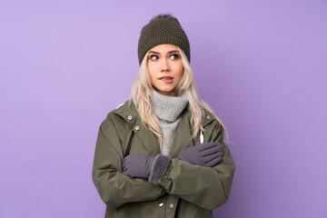 Teenager blonde girl with winter hat over isolated purple background with confuse face expression