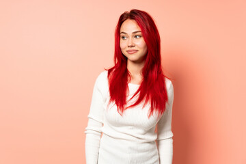 Obraz premium Teenager red hair girl isolated on pink background making doubts gesture looking side