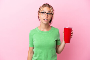 Young Russian woman holding a refreshment isolated on pink background looking up and with surprised...