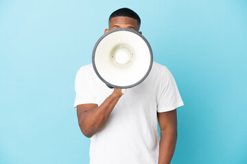 Young latin man isolated on blue background shouting through a megaphone to announce something