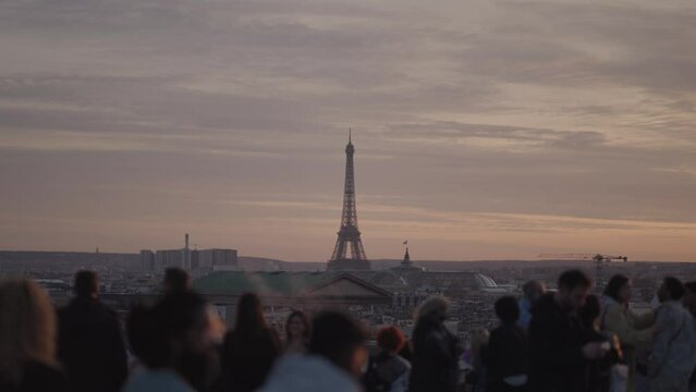 Unrecognizable Tourists on the rooftop of Galeries Lafayette Haussmann enjoying the sunset with the iconic Eiffel Tower and the city buildings of Paris in the background