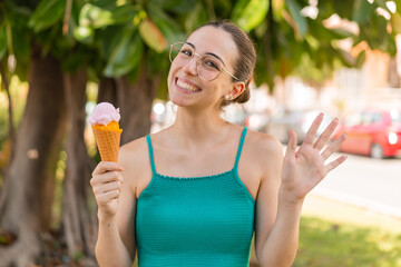 Young pretty woman with a cornet ice cream at outdoors saluting with hand with happy expression