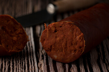 On a rustic wooden table, typical Mallorcan sausage (sobrassada) cut into two pieces with a knife specifically designed for this purpose.