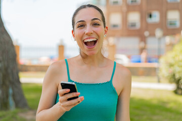 Young pretty woman using mobile phone at outdoors with surprise and shocked facial expression