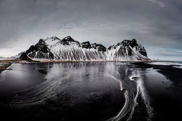 Snow-covered Vestrahorn mountains reflecting in icy waters at Stokksnes beach, South East Iceland.
