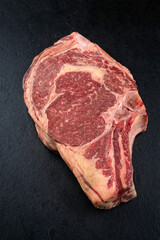 Raw dry aged chianina rib of beef steak offered as close-up on a black design board