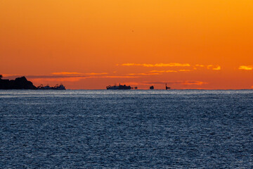 Silhouettes of fishing boats, waiting to set sail, illuminated by the dawn sun on the horizon line...