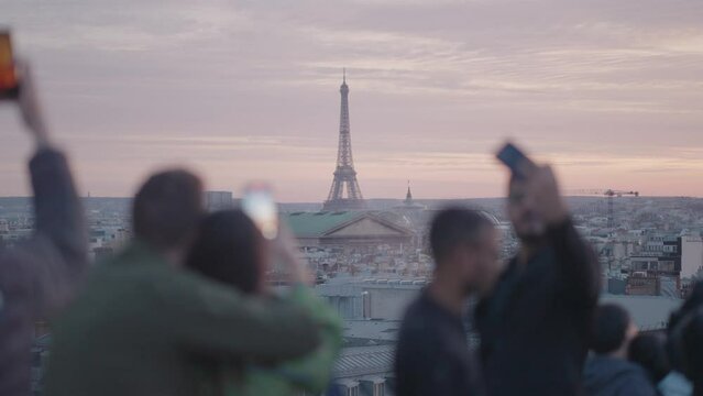 Unrecognizable Tourists on the rooftop of Galeries Lafayette Haussmann enjoying the sunset with the iconic Eiffel Tower and the city buildings of Paris in the background