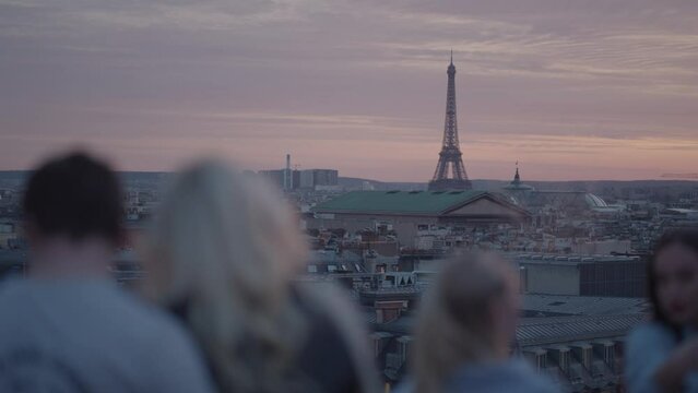 Unrecognizable Tourists on the rooftop of Galeries Lafayette Haussmann enjoying the sunset with the iconic Eiffel Tower and the city buildings of Paris in the background