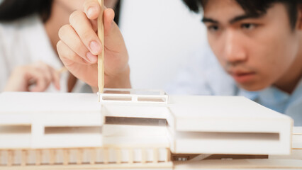 Closeup of young professional architect team work together to use pencil testing house model...