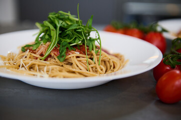 Italian pasta. Fresh homemade spaghetti capellini pasta with tomato sauce and garnished with arugula green leaves on the kitchen table near a branch of organic tomato cherry