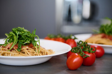 A served dish with delicious Italian pasta with the tomato sauce, seasoned with fresh arugula leaves and grated parmesan cheese on the pasta in a plate. Decoration of dish