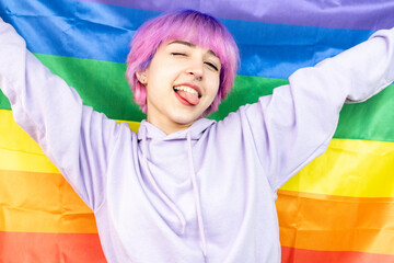 A woman with pink hair is holding a rainbow flag. She is smiling and she is happy. LGBT young woman...