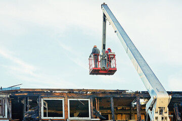 Workers on crane cradle dismantle burnt roof after fire, team effort in the cleanup and...
