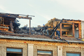 Unrecognizable  construction team dismantle charred roof in the aftermath of fire. Post-fire...