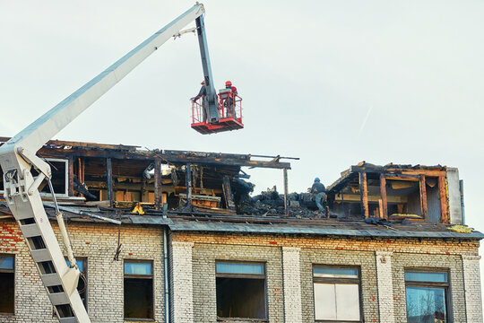 Unrecognizable workers in crane cradle dismantling charred roof after fire, aftermath of an emergency. Men cleanup and restoration building roof after fire..