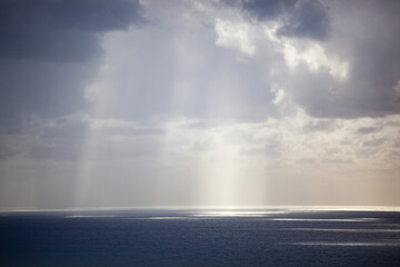 Overcast grey sky with low textured clouds. Sunlight peeks through the clouds and falls on the sea. Background. Horizontal